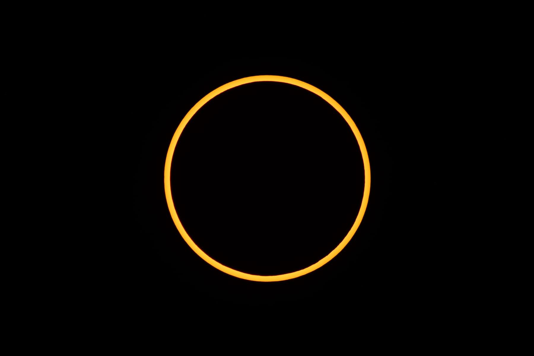 Schmaler, hell orangefarbener Sonnenring um den dunklen Mond vor schwarzem Himmel