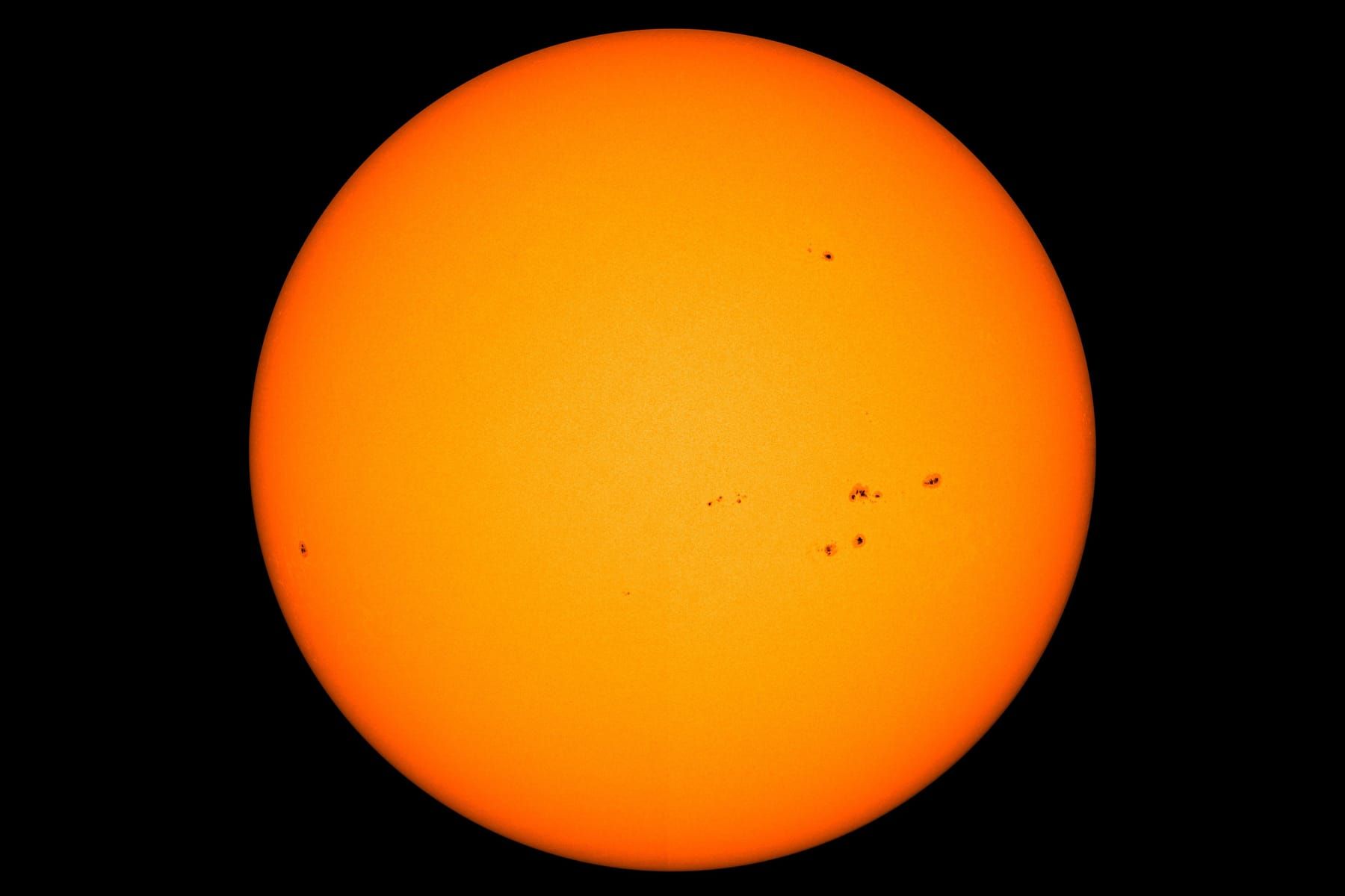 Full orange disc of the Sun with several small groups of dark sunspots